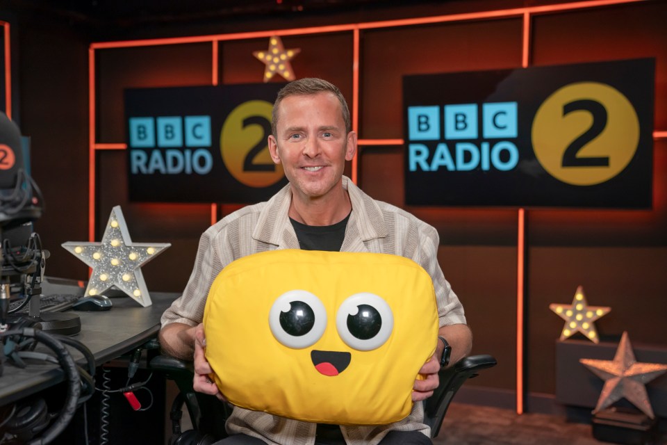 a man holds a yellow pillow in front of a bbc radio 2 sign
