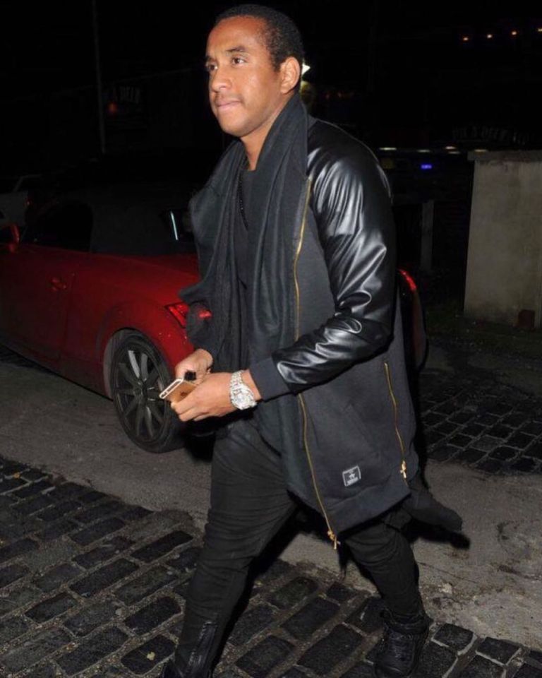 a man wearing a black jacket with leather sleeves walks down a cobblestone street