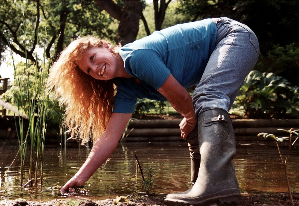 a woman wearing rubber boots is bending over in the water