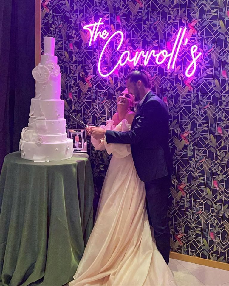 a bride and groom are cutting their wedding cake under a neon sign that says the carroll 's
