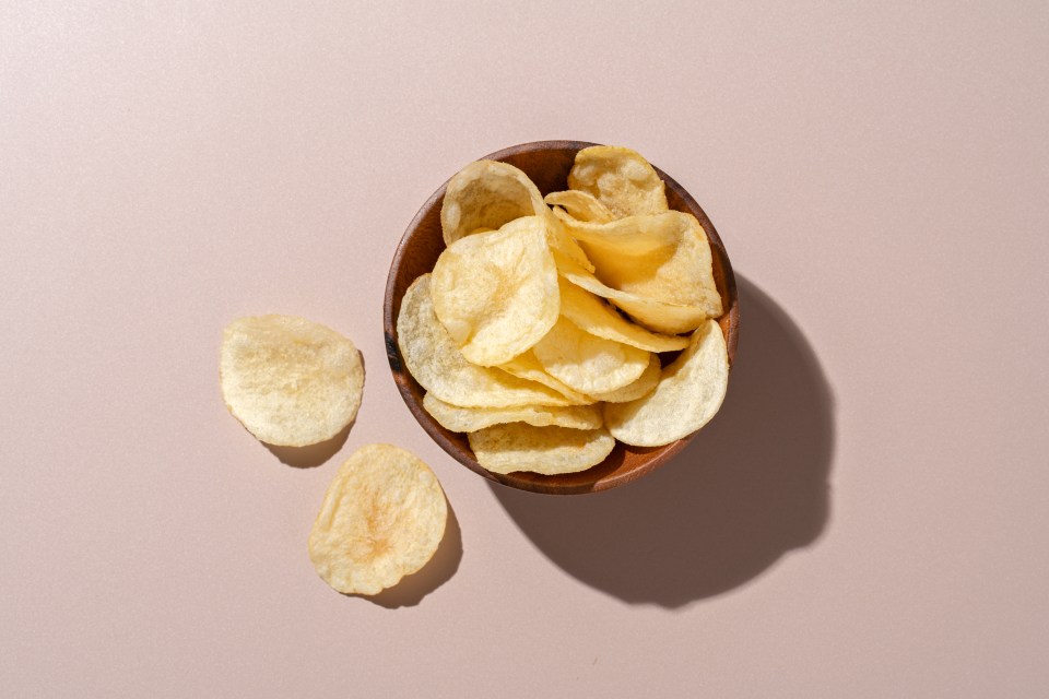 a wooden bowl filled with potato chips on a pink background