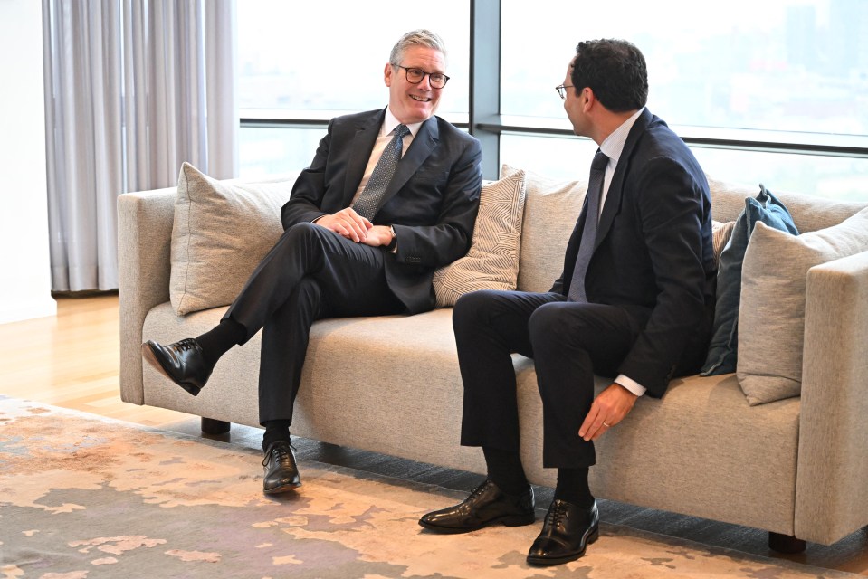 two men in suits sit on a couch talking