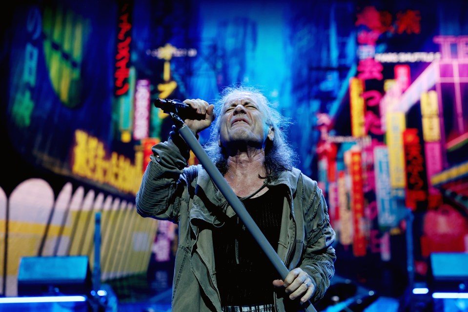 a man singing into a microphone in front of a neon sign that says ' tokyo '