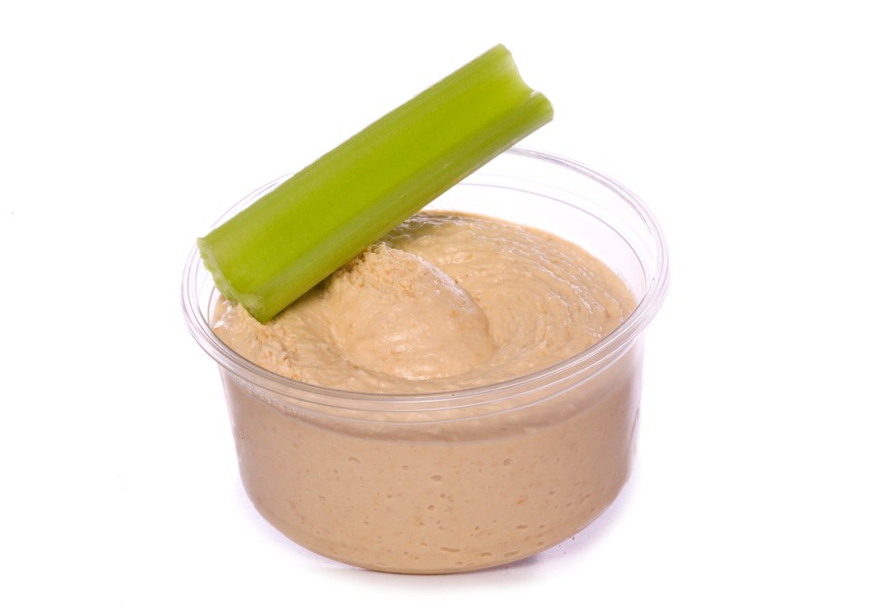 a cup of hummus with a celery stick sticking out of it