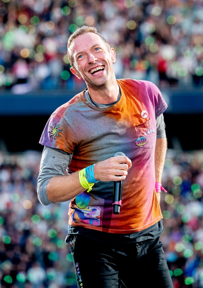a man wearing a tie dye shirt holds a microphone and smiles