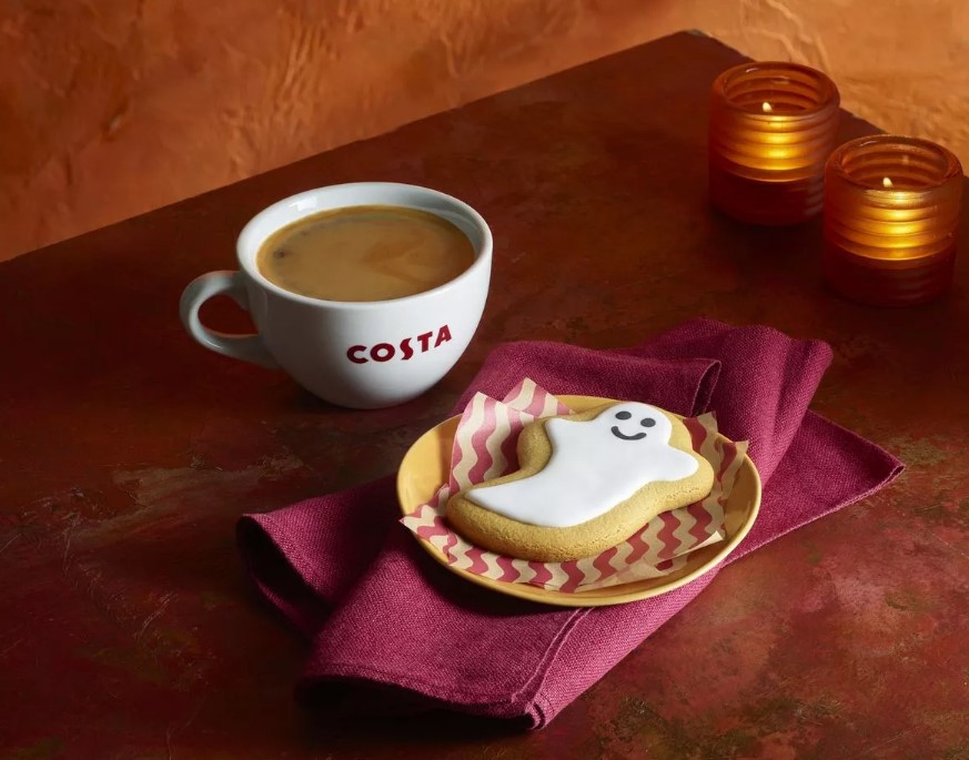 a cup of costa coffee and a ghost cookie on a plate