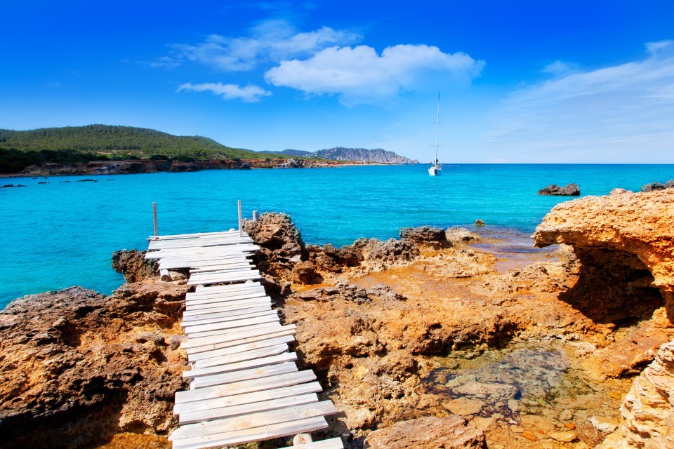 a wooden dock leads to the ocean with a sailboat in the distance