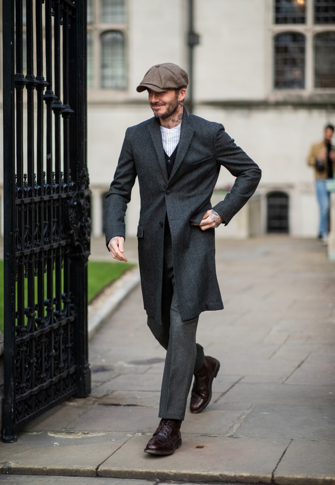 a man wearing a hat and a grey coat walks down a sidewalk