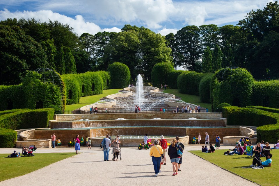 a group of people walking around a fountain in a park
