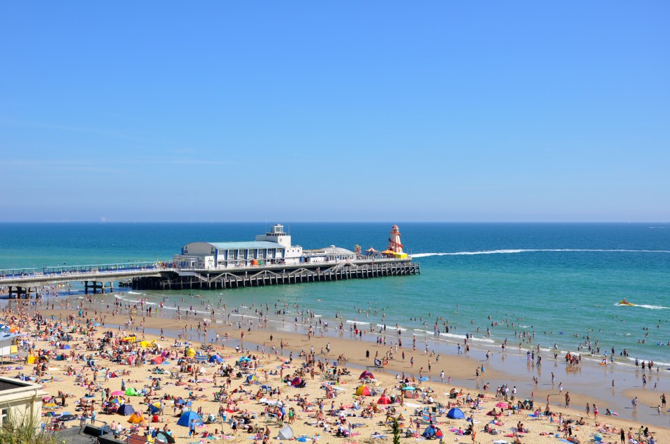 a crowded beach with a lighthouse in the background
