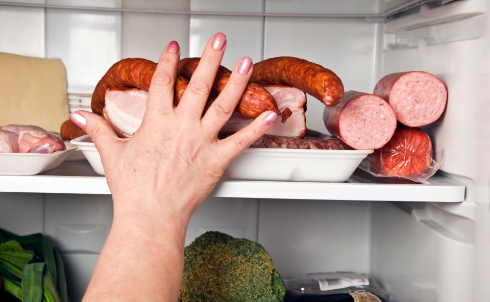 a woman 's hand is reaching into a refrigerator filled with meat and sausages