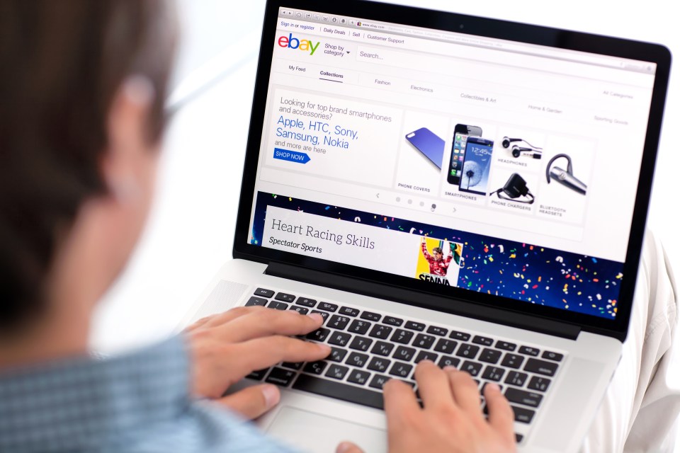 a man is typing on a laptop that is open to ebay