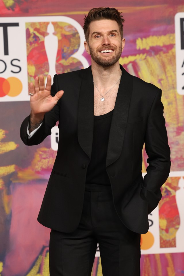 a man in a black suit is waving at the camera