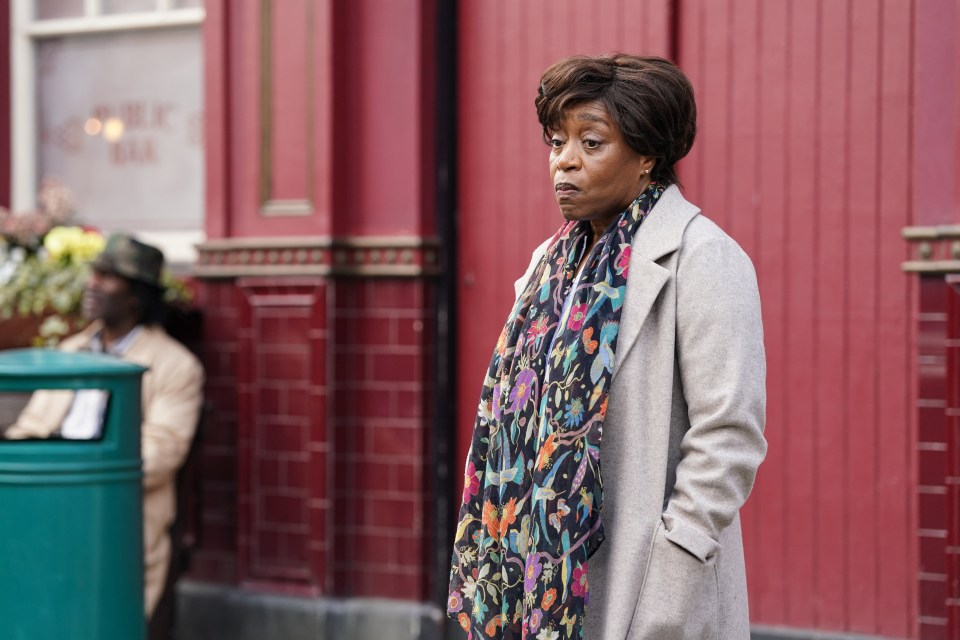 a woman wearing a scarf stands in front of a red building