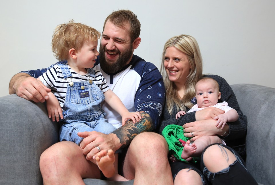a family sitting on a couch with a baby wearing overalls