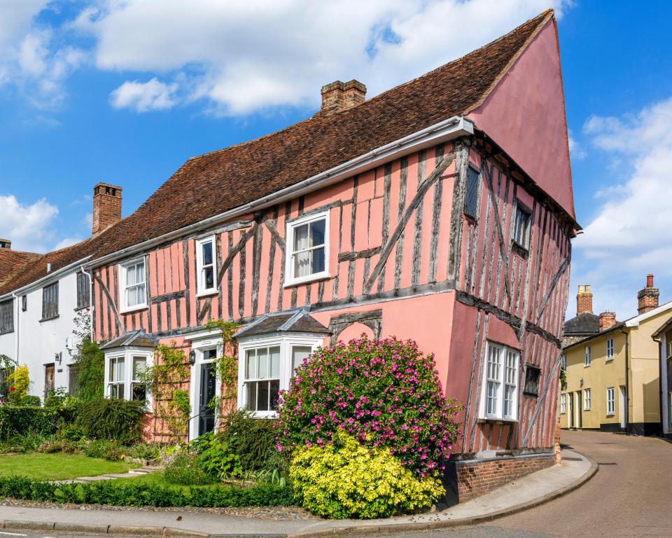 a pink house with a wooden frame sits on the corner of a street