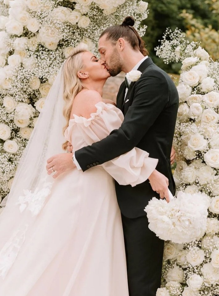 a bride and groom kissing in front of a wall of white flowers