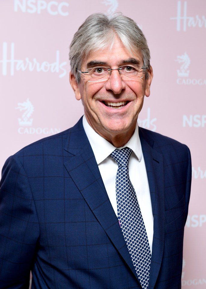 a man in a suit and tie smiles in front of a harrods sign
