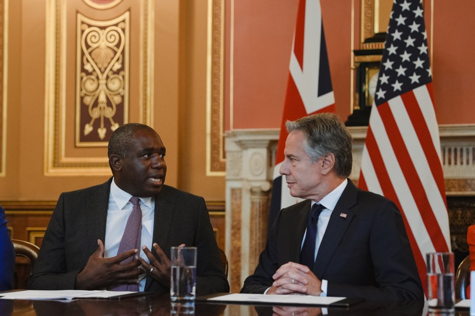 two men sit at a table with flags in the background