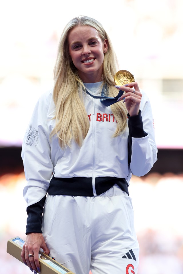 a woman holding a gold medal with the word brit on her jacket