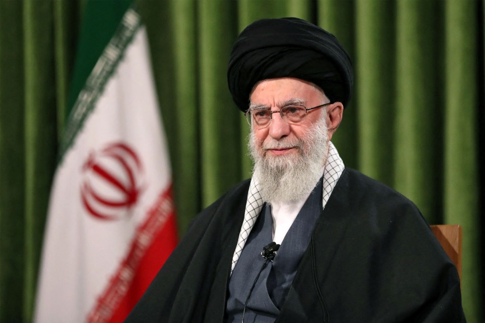 a man with glasses and a beard is sitting in front of an iranian flag