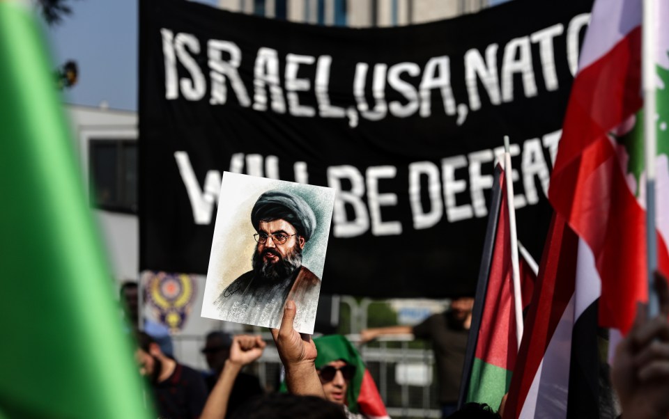 a man holds up a picture of a man in front of a banner that says israel usa nato will be defeated