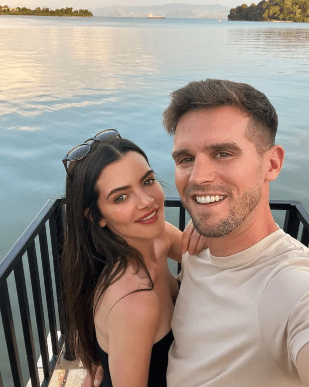 a man and a woman are posing for a picture in front of a body of water