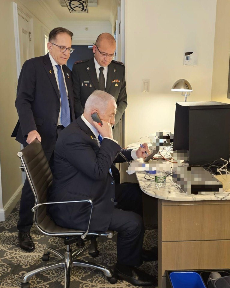 a man in a suit sits at a desk talking on a cell phone