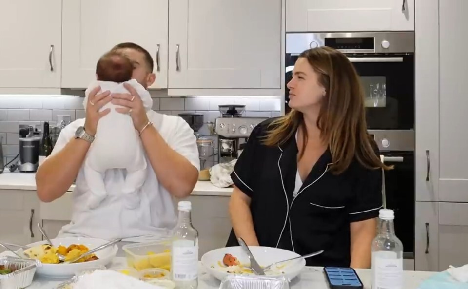 a man is holding a baby while a woman looks on