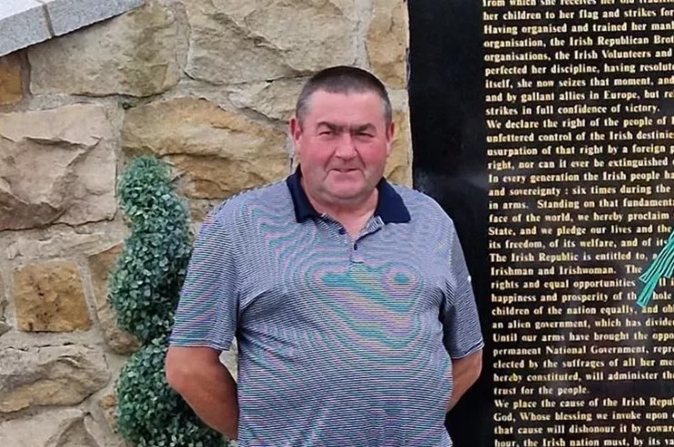 a man stands in front of a stone wall with a plaque on it