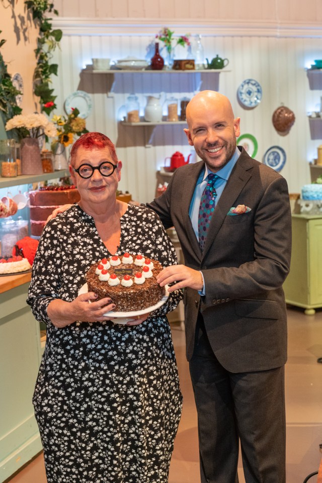 a man in a suit stands next to a woman holding a cake