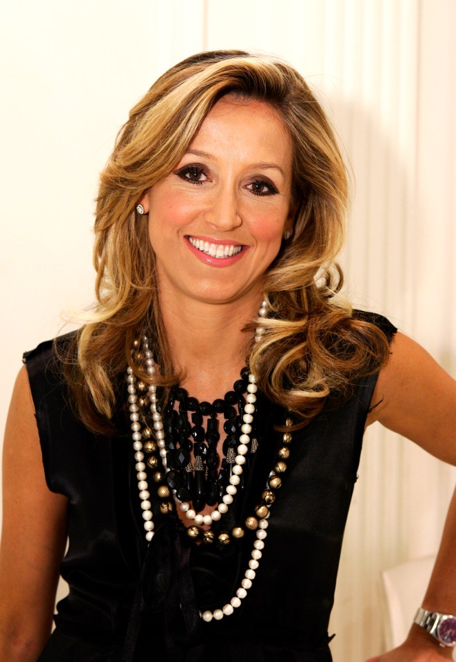 a woman wearing a black top and a pearl necklace smiles for the camera