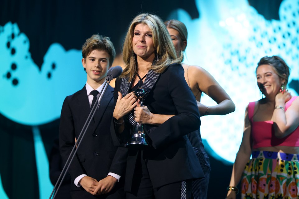 a woman in a black suit holds a trophy in front of a microphone