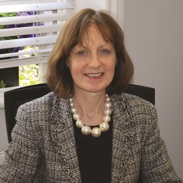 a woman wearing a pearl necklace is smiling for the camera