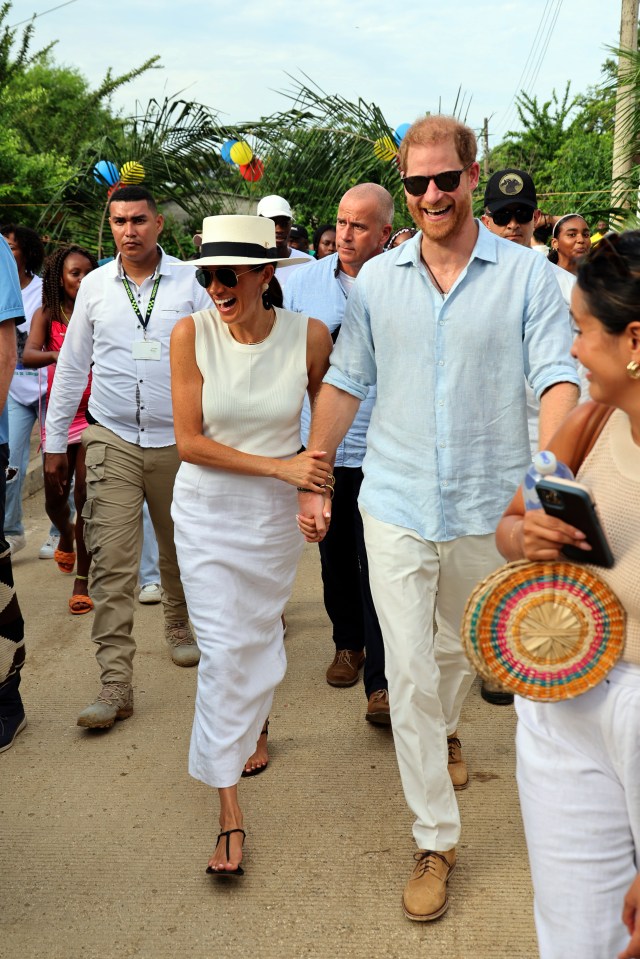 prince harry and meghan markle walk down a street holding hands