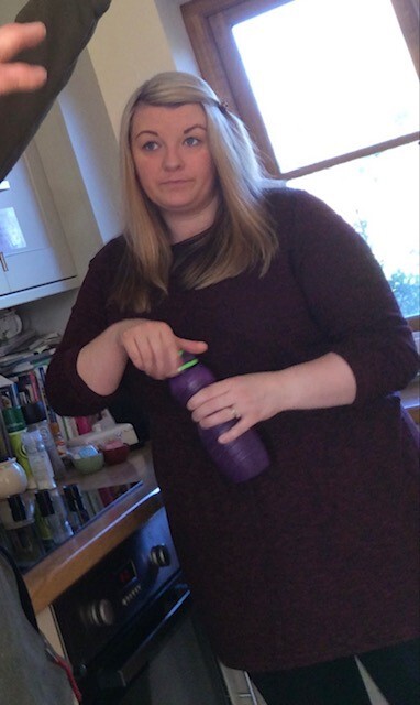 a woman standing in a kitchen holding a purple bottle