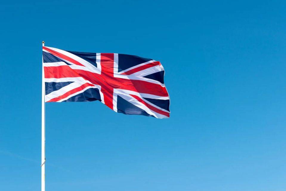 a british flag is flying in the wind against a blue sky
