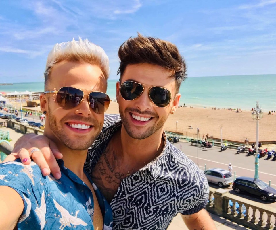two men in white shirts and suspenders pose for a picture on the beach