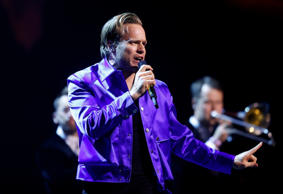 a man in a purple jacket sings into a microphone