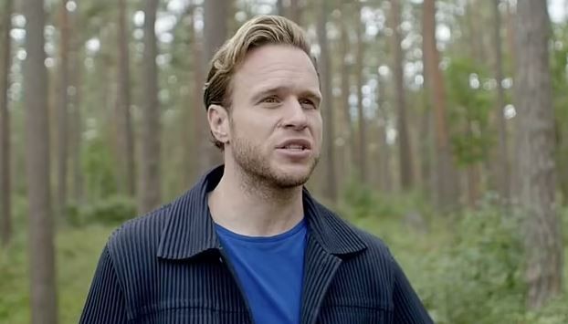 a man in a blue shirt and black jacket is standing in a forest .