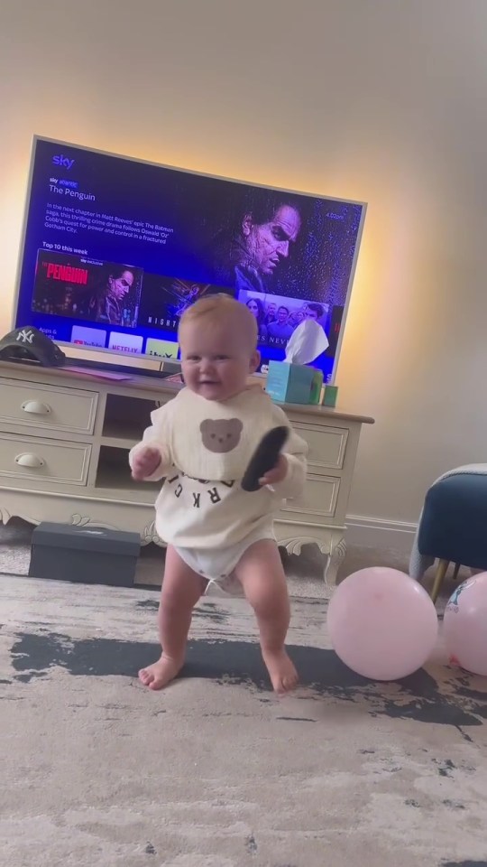 a baby is standing in front of a sky tv