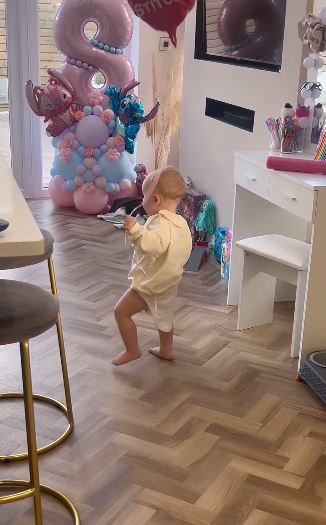 a baby is standing on a wooden floor in a room with balloons .