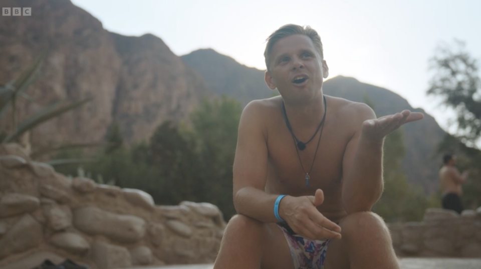 a shirtless man sits in front of a bbc logo