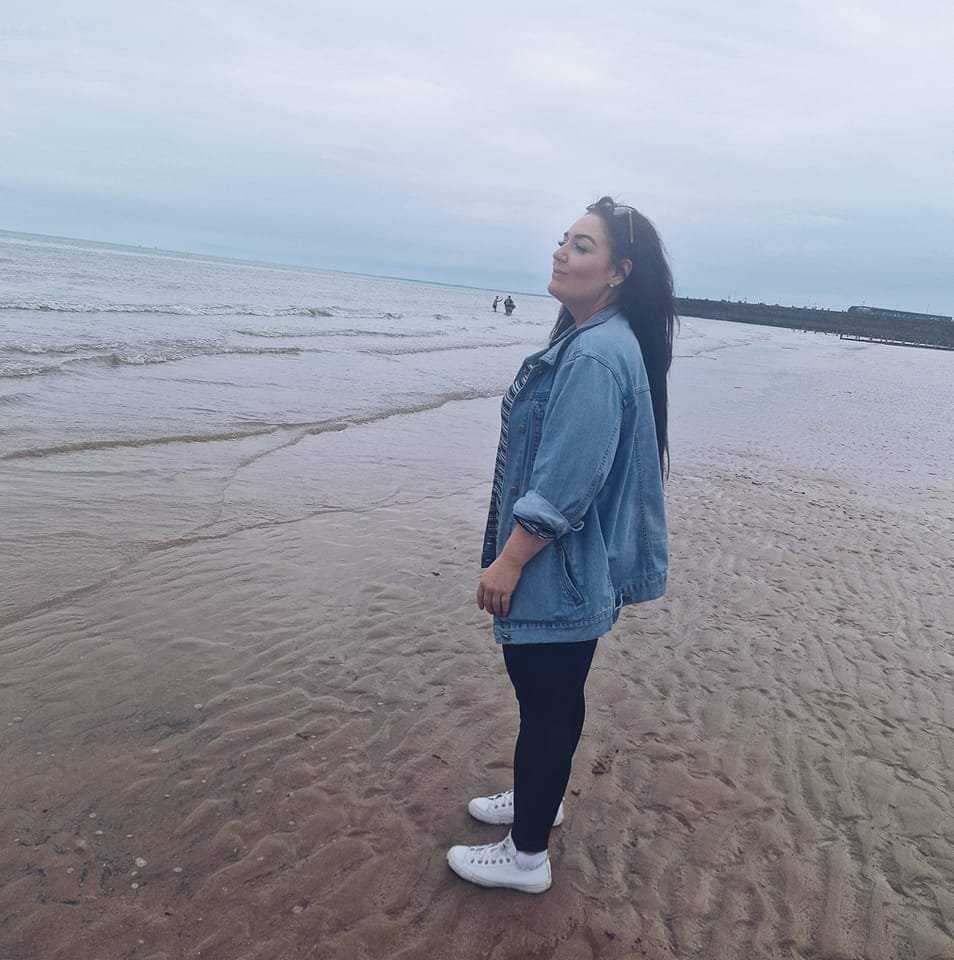 a woman in a denim jacket is standing on a beach