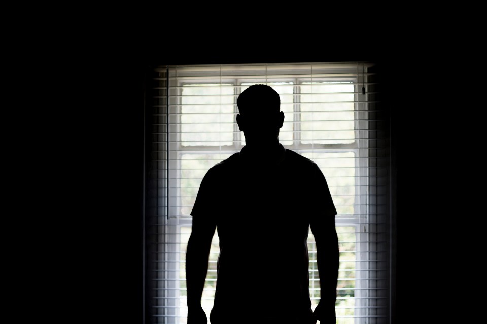 a silhouette of a man standing in front of a window with blinds