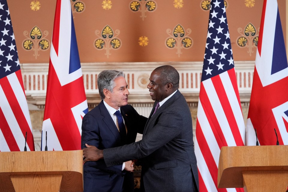 two men shaking hands in front of american and british flags