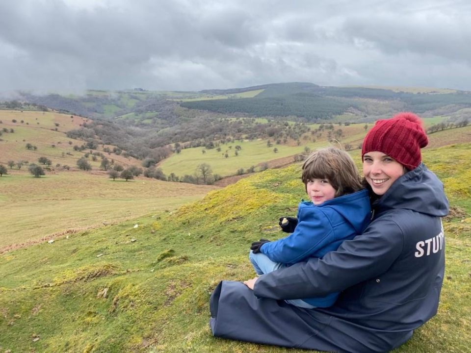a woman and child are sitting on top of a hill and the woman is wearing a jacket that says stud