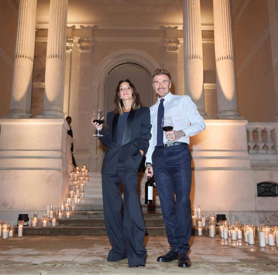 a man and a woman standing in front of a building holding wine glasses