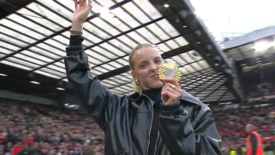 a woman is holding a gold medal in her hands on a soccer field .