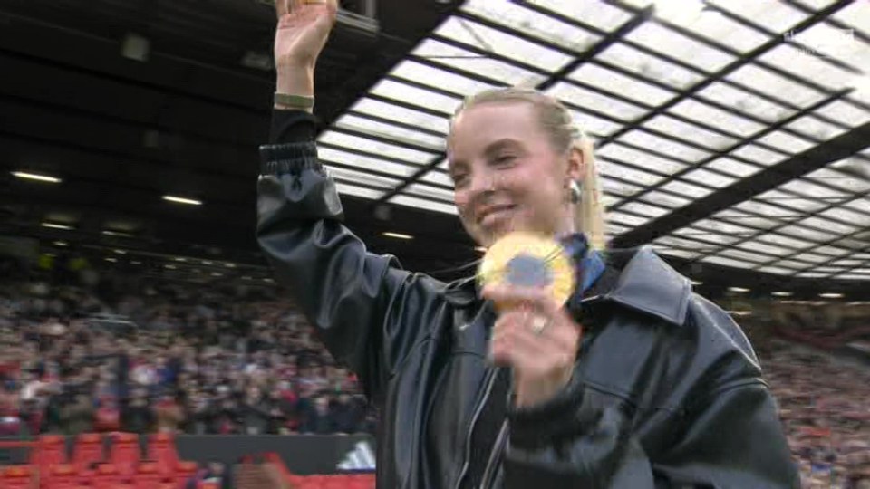 a woman in a leather jacket is holding a gold medal in a stadium .